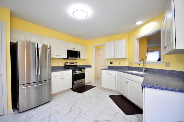 kitchen featuring white cabinets, dark countertops, appliances with stainless steel finishes, marble finish floor, and a sink