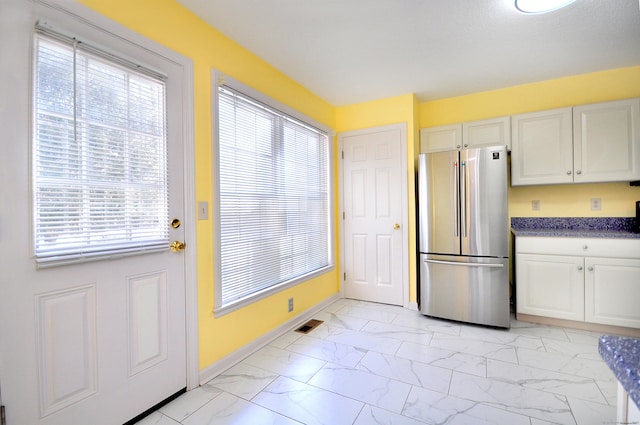 interior space featuring visible vents, marble finish floor, freestanding refrigerator, and white cabinetry