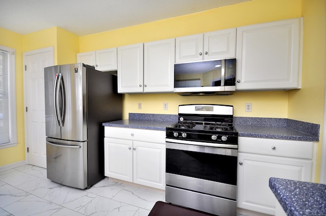 kitchen featuring stainless steel appliances, dark countertops, marble finish floor, and white cabinetry