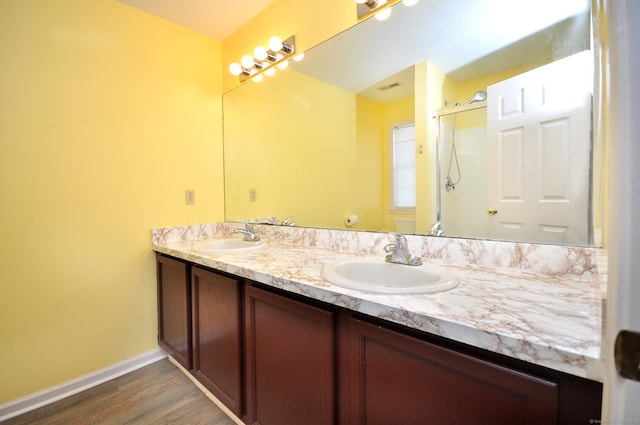 full bath with wood finished floors, a shower with shower door, a sink, and double vanity