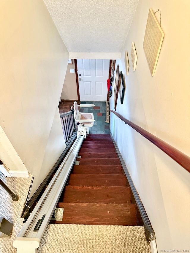 stairs with a textured ceiling, wood finished floors, and baseboards