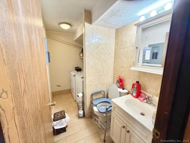 bathroom with a textured ceiling, separate washer and dryer, vanity, tile walls, and tile patterned floors