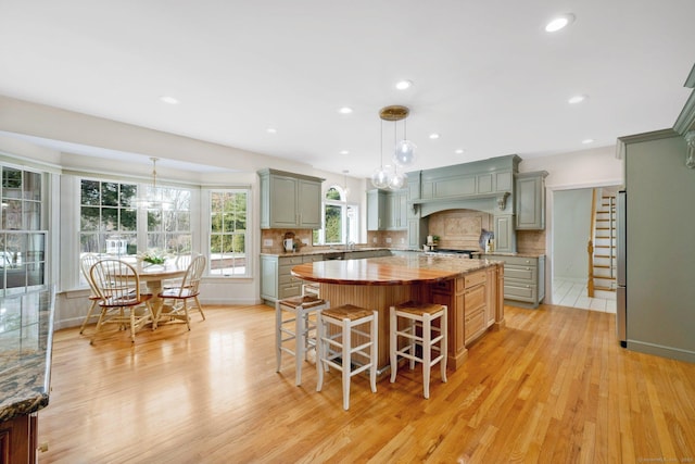 kitchen with a kitchen bar, gray cabinetry, a kitchen island, light wood finished floors, and decorative backsplash