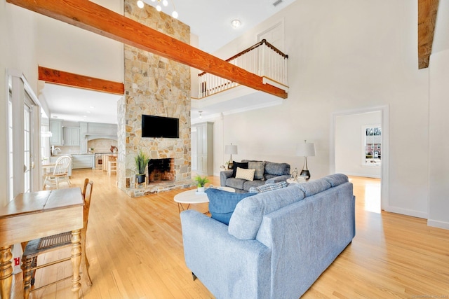 living room featuring plenty of natural light, a high ceiling, a stone fireplace, and wood finished floors