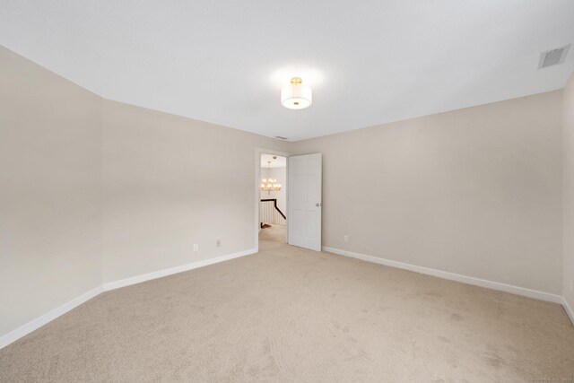 spare room featuring a notable chandelier, visible vents, light colored carpet, and baseboards