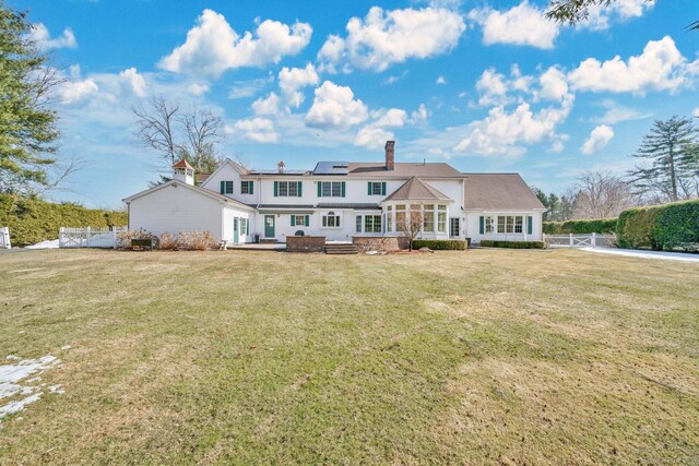 view of front of house with a front lawn, a gate, fence, solar panels, and a chimney