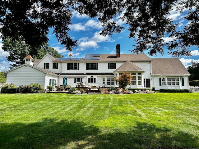 rear view of property featuring solar panels, a lawn, and a chimney