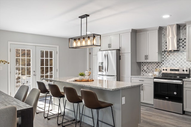 kitchen with french doors, gray cabinetry, appliances with stainless steel finishes, a kitchen island, and wall chimney range hood