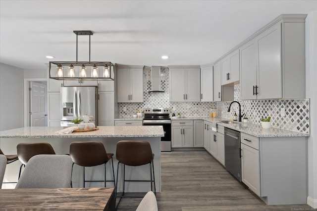 kitchen with stainless steel appliances, a sink, a kitchen breakfast bar, wall chimney exhaust hood, and tasteful backsplash