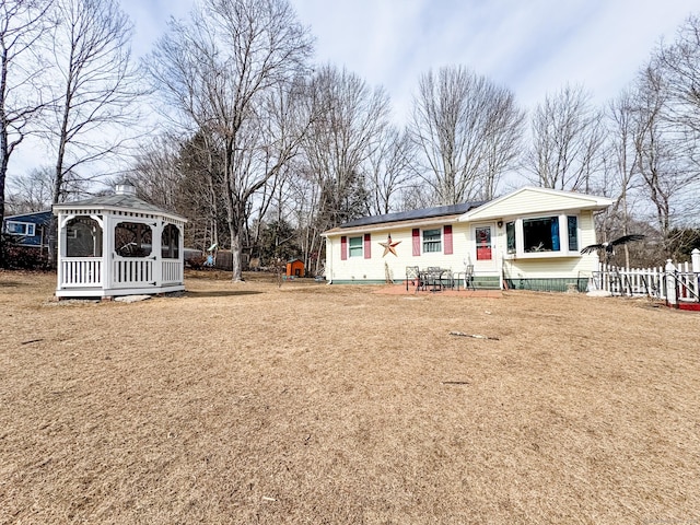 view of front of property with roof mounted solar panels, fence, a front lawn, and a gazebo