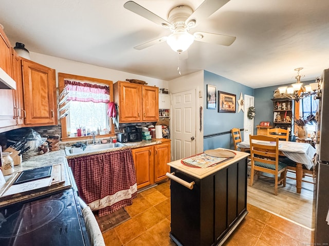 kitchen with light countertops, a sink, backsplash, and ceiling fan with notable chandelier