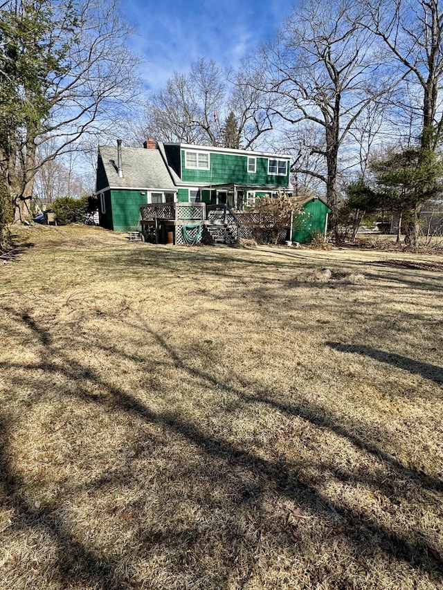 rear view of property featuring a deck, a yard, stairs, and a chimney