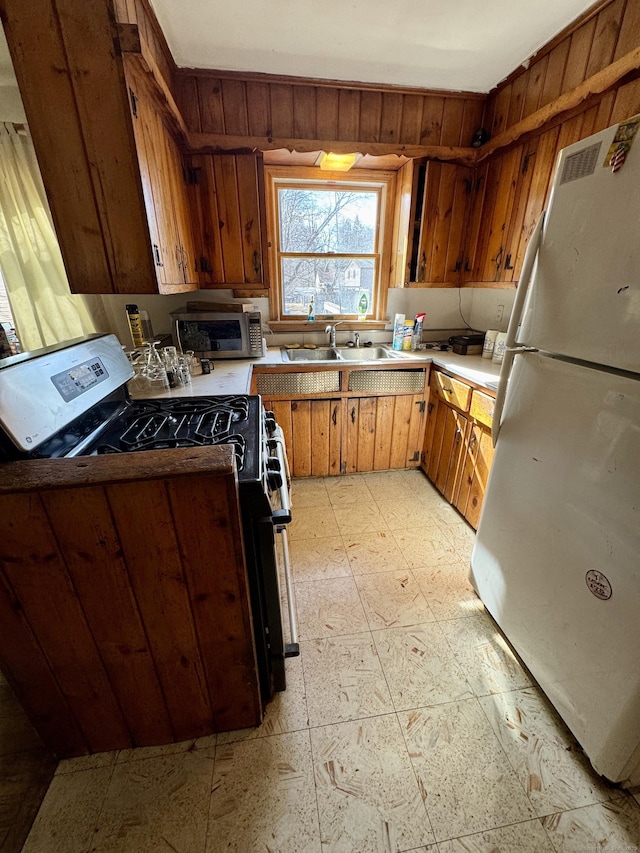 kitchen featuring gas stove, light floors, freestanding refrigerator, a sink, and wood walls