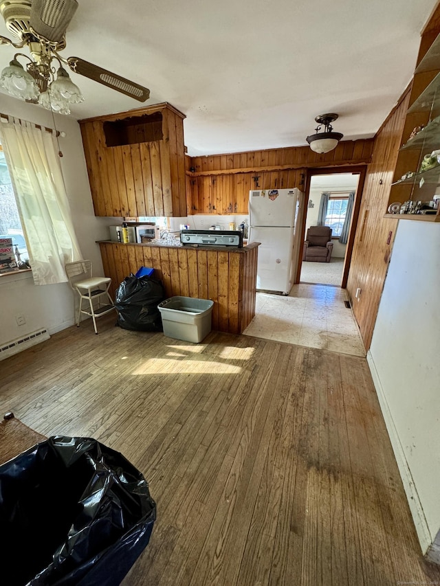 kitchen featuring light wood finished floors, a baseboard heating unit, a peninsula, freestanding refrigerator, and brown cabinetry