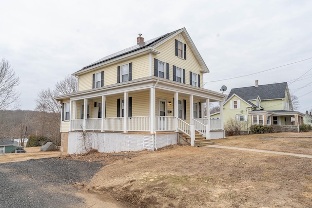 farmhouse with a chimney, a porch, and roof mounted solar panels