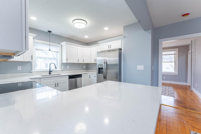 kitchen with light wood finished floors, stainless steel appliances, hanging light fixtures, white cabinets, and a sink