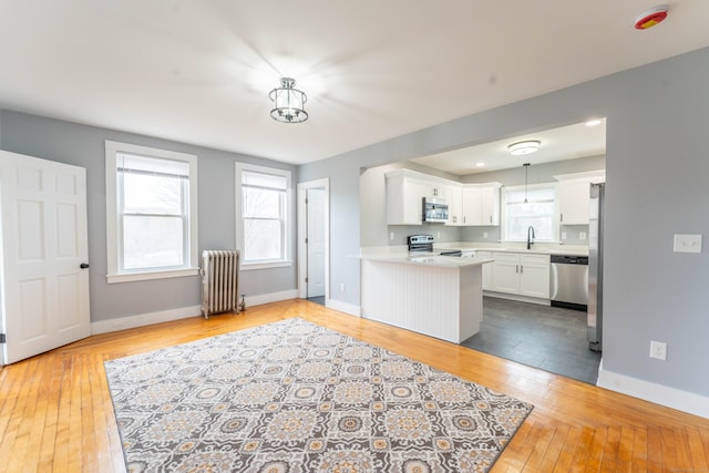 kitchen with stainless steel appliances, white cabinetry, light countertops, light wood finished floors, and radiator heating unit