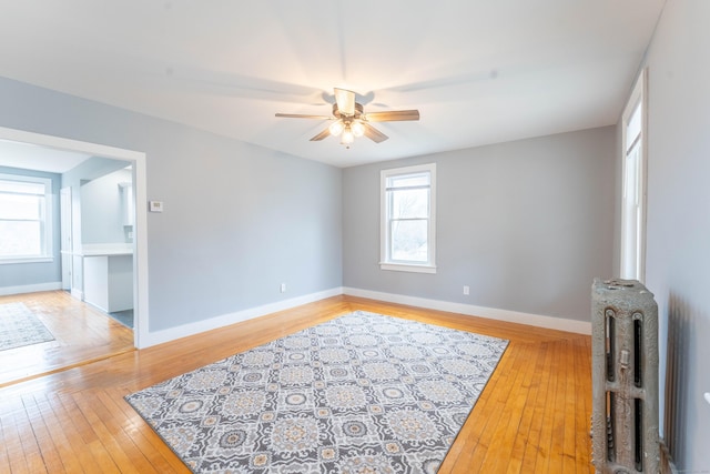 living area with a ceiling fan, radiator heating unit, light wood-style flooring, and baseboards