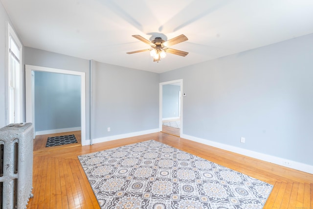 interior space with baseboards, light wood-type flooring, a ceiling fan, and radiator