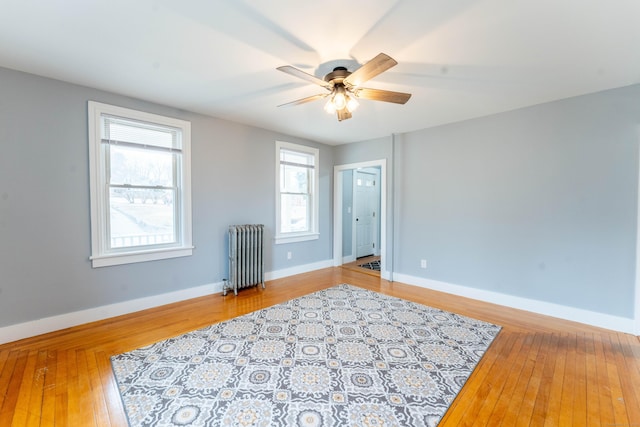 unfurnished room with hardwood / wood-style floors, radiator heating unit, a ceiling fan, and baseboards