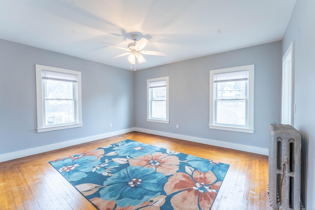 spare room featuring baseboards, ceiling fan, wood-type flooring, and radiator