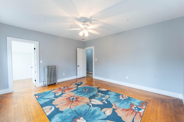 spare room featuring a ceiling fan, radiator, baseboards, and hardwood / wood-style flooring