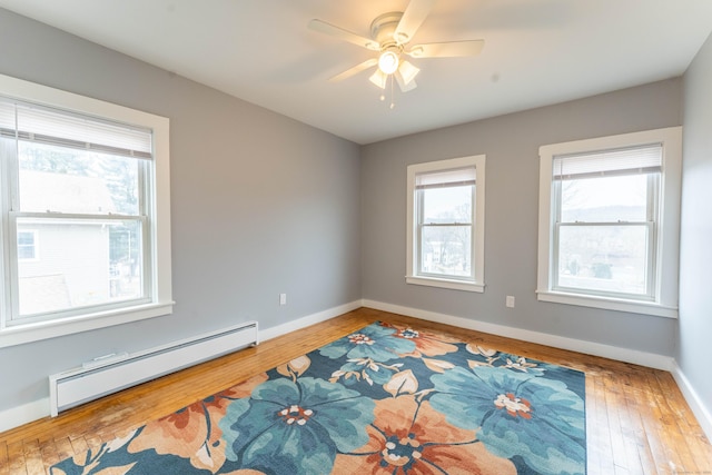 unfurnished room with a baseboard heating unit, hardwood / wood-style floors, plenty of natural light, and baseboards