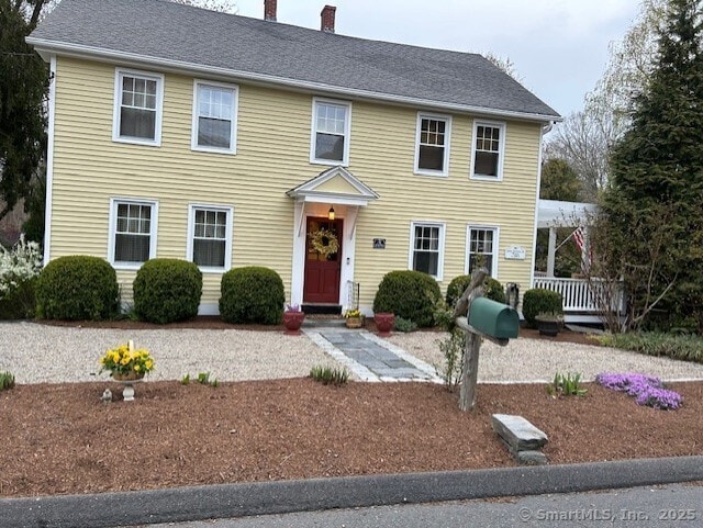 colonial inspired home with a chimney and roof with shingles