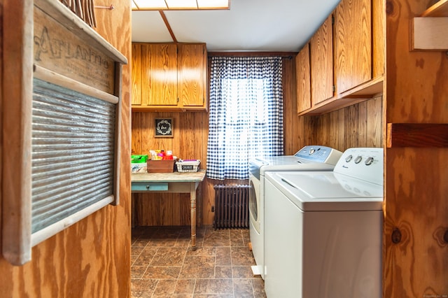 laundry room with wooden walls, radiator heating unit, cabinet space, stone finish floor, and washing machine and dryer