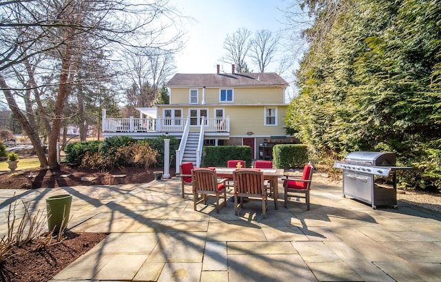 rear view of house with stairway, outdoor dining area, a patio, and a deck