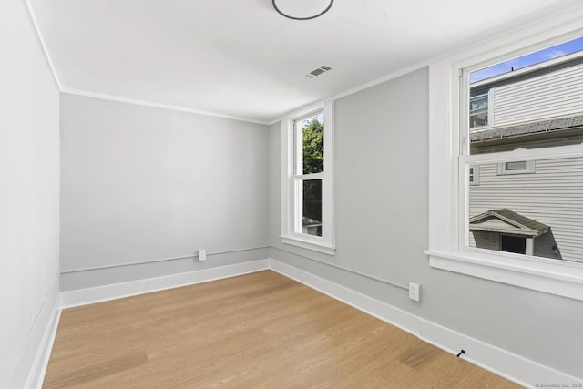 empty room featuring ornamental molding, wood finished floors, visible vents, and baseboards