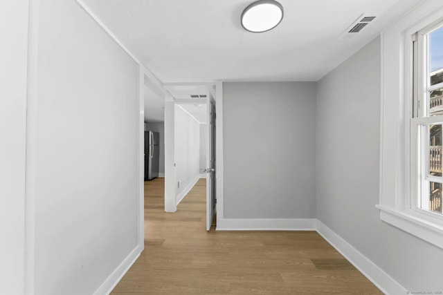 corridor with light wood finished floors, visible vents, and baseboards