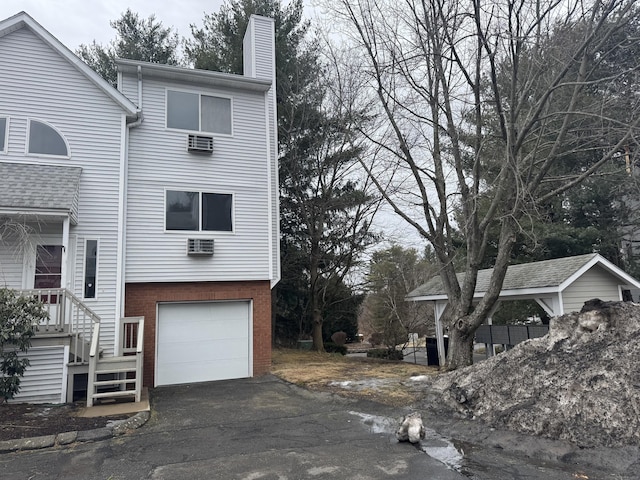 view of property exterior featuring an attached garage, a chimney, aphalt driveway, and brick siding