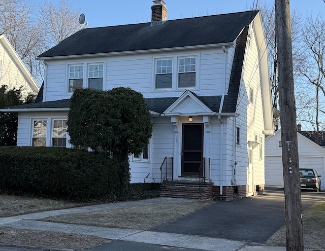 view of front of house with entry steps, a shingled roof, a chimney, and an outdoor structure