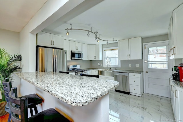 kitchen with marble finish floor, stainless steel appliances, a kitchen bar, white cabinetry, and a sink