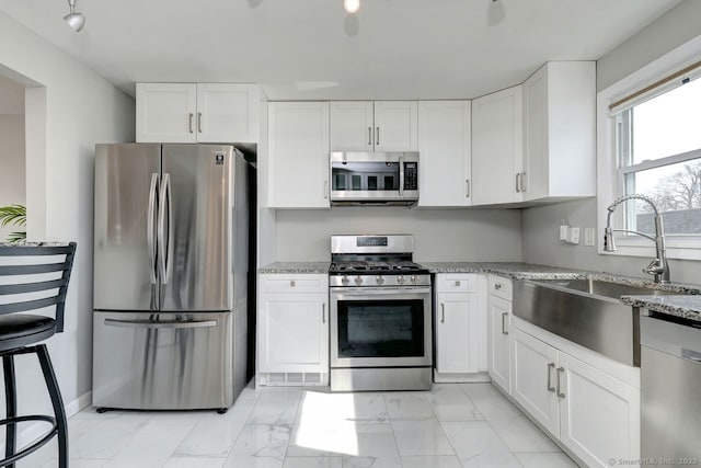 kitchen featuring light stone counters, stainless steel appliances, a sink, white cabinets, and marble finish floor