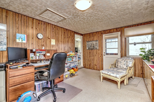 carpeted home office with wood walls and attic access