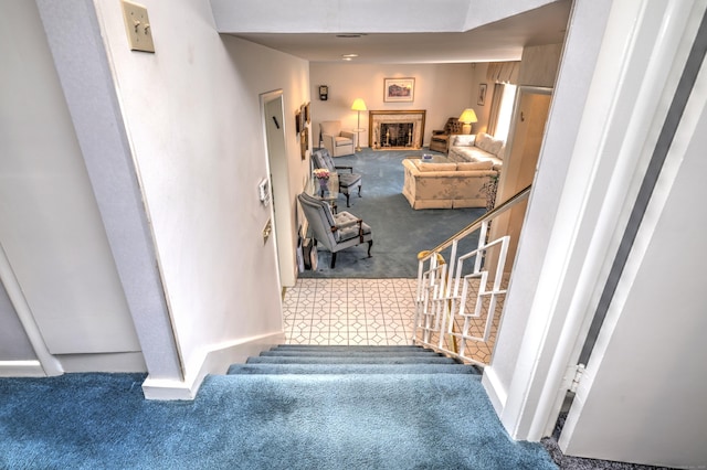 staircase featuring a fireplace with raised hearth and carpet floors