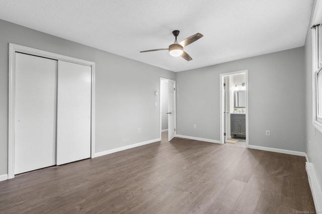 unfurnished bedroom with baseboards, connected bathroom, ceiling fan, dark wood-style flooring, and a closet