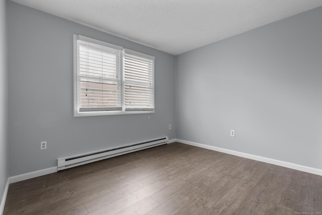 empty room with a baseboard heating unit, wood finished floors, and baseboards