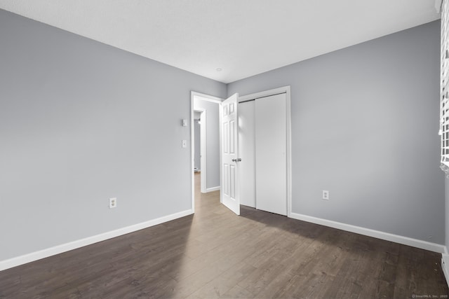 unfurnished bedroom featuring dark wood-style flooring, a closet, and baseboards