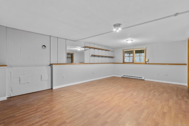 spare room with concrete block wall, baseboards, a baseboard heating unit, and wood finished floors