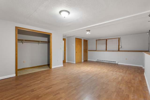 unfurnished bedroom with a baseboard radiator, baseboards, light wood-style flooring, and a textured ceiling