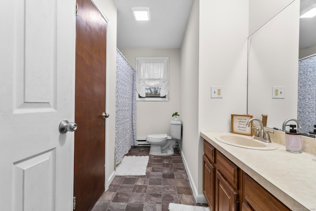 bathroom with toilet, a baseboard heating unit, stone finish floor, vanity, and baseboards