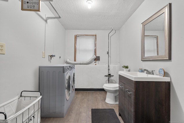 bathroom with a textured ceiling, toilet, wood finished floors, vanity, and washing machine and clothes dryer