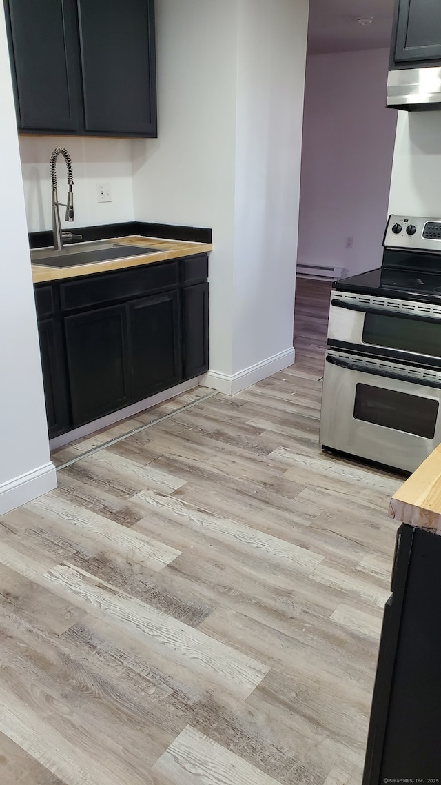 kitchen with light wood-style flooring, under cabinet range hood, baseboards, double oven range, and a sink