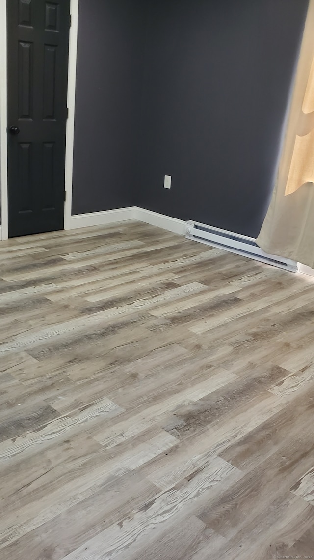 empty room with wood finished floors, baseboards, and a baseboard heating unit
