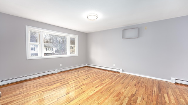 empty room with a baseboard heating unit, baseboards, and wood finished floors