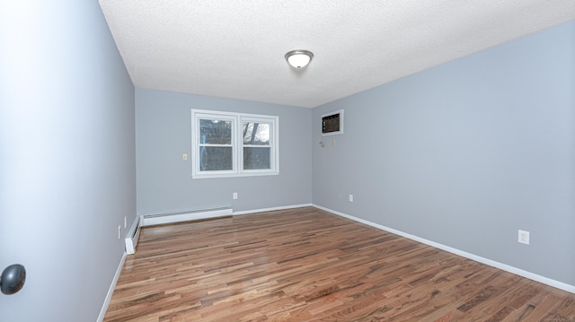 spare room featuring a textured ceiling, baseboard heating, wood finished floors, and baseboards