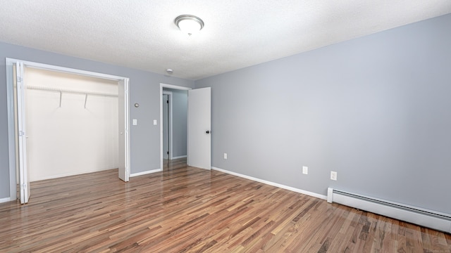 unfurnished bedroom featuring a baseboard radiator, a closet, a textured ceiling, and wood finished floors